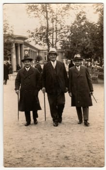 LAZNE PODEBRADY, THE CZECHOSLOVAK REPUBLIC - CIRCA 1930s: Vintage photo shows the elegant men at the spa resort. They wear hats and hold walking sticks. Colonnade is on background.