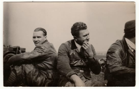 THE CZECHOSLOVAK SOCIALIST REPUBLIC - CIRCA 1950s: Vintage photo shows men wear leather jacket and vest. Men have a rest after car trip. Black & white antique photography.