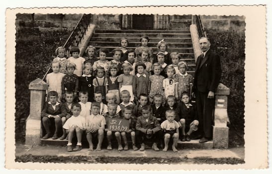 THE CZECHOSLOVAK REPUBLIC - 1939: Vintage photo shows pupils (schoolmates) and their teacher pose in front of school. Black & white antique photography.