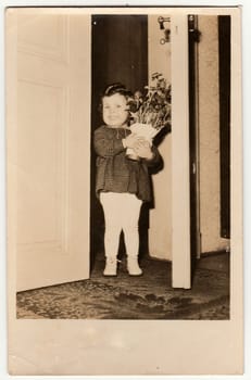 THE CZECHOSLOVAK REPUBLIC - CIRCA 1950s: Vintage photo shows a cute small girl holds the vase with flowers. Retro photography.