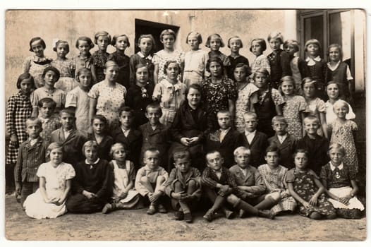 THE CZECHOSLOVAK REPUBLIC - SEPTEMBER 30, 1936: Vintage photo shows pupils (schoolmates) and their schoolmistress pose in front of school. Black & white antique photography.