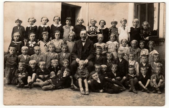 THE CZECHOSLOVAK REPUBLIC - SEPTEMBER 30, 1939: Vintage photo shows pupils (schoolmates) and their teacher pose in front of school. Black & white antique photography.