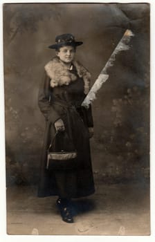 PRAHA PRAGUE , THE CZECHOSLOVAK REPUBLIC - NOVEMBER 1, 1918: The vintage photo shows young woman wears an elegant coat with fur scarf, ladies wide-brimmed hat and holds handbag. The studio photography with sepia effect was taken in pre-twenties.