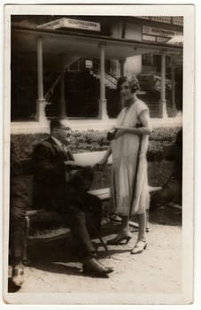 KARLOVY VARY, THE CZECHOSLOVAK REPUBLIC - CIRCA 1930s: Vintage photo shows the elegant man and woman at the spa resort. Men wear slack suits, woman white dress. Colonnade is on background.