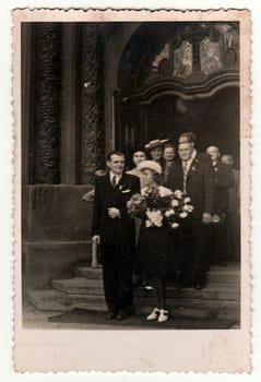 PRAHA PRAGUE , THE CZECHOSLOVAK SOCIALIST REPUBLIC - CIRCA 1950s: Retro photo shows the newlyweds and wedding guests on stairs of cathedral church . Black white photography.