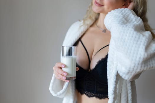 sexy young woman in black lingerie pouring milk on body isolated on grey.