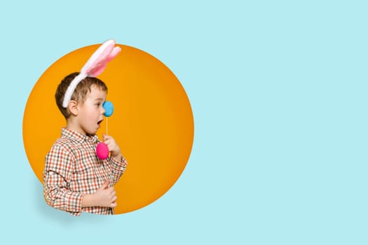 cute little child boy with Easter bunny ears holding colorful eggs on yellow and blue background. Happy easter. copy space