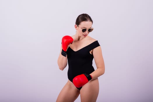 Seductive female boxer with athletic beautiful figure in black swimsuit gloves on a gray background