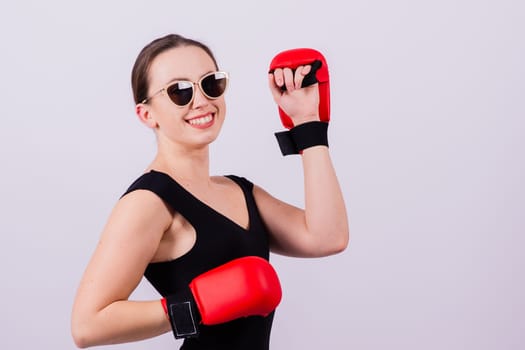 Seductive female boxer with athletic beautiful figure in black swimsuit gloves on a gray background