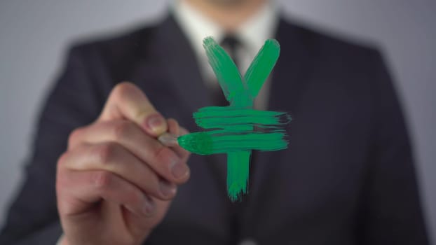 A businessman draws the yuan currency symbol on the glass. A man in a suit draws on glass with a brush and green paint. 4k