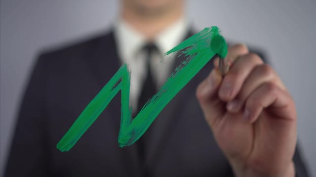 Businessman draws a market growth graph. A man in a suit draws on glass with a brush and green paint. 4k