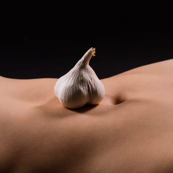 Close up of a woman belly with laying garlic, low key