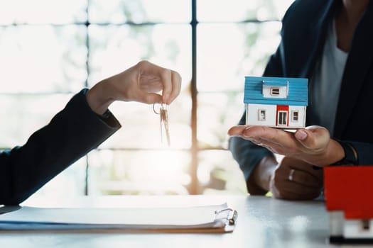 Accountant, businessman, real estate agent, Asian business woman handing keys to customers along with house after customers to sign.