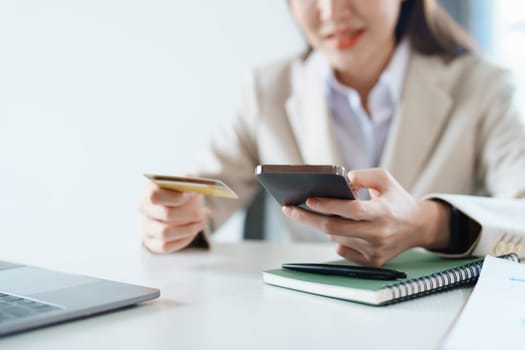 Portrait of young Asian woman using credit card and phone for online shopping.