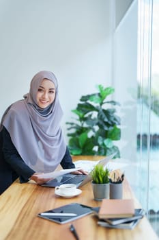 A beautiful Muslim woman showing a smiling face in the morning using computers and documents working at the office.