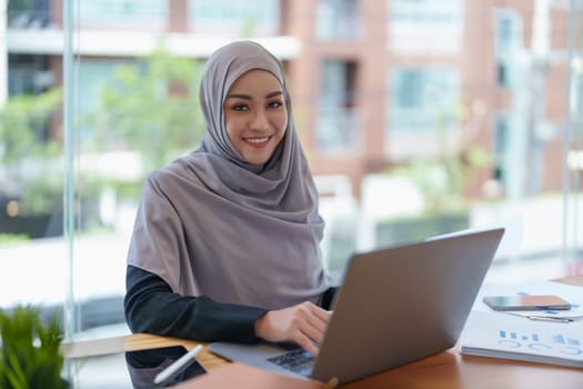 A beautiful Muslim woman showing a smiling face in the morning using computers and documents working at the office.