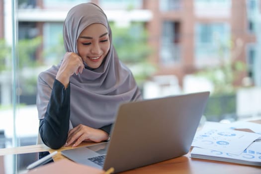 A beautiful Muslim woman showing a smiling face in the morning using computers and documents working at the office.