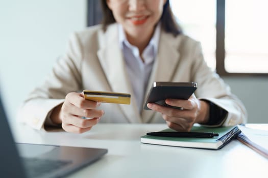 Portrait of young Asian woman using credit card and phone for online shopping.