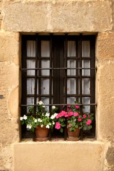 A window of a rustic house with railings and flowerpots,Coloured flowers, wrought iron, white curtains, stone, etc.