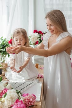 A little blonde girl with her mom on a kitchen countertop decorated with peonies. The concept of the relationship between mother and daughter. Spring atmosphere