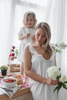 A little blonde girl with her mom on a kitchen countertop decorated with peonies. The concept of the relationship between mother and daughter. Spring atmosphere