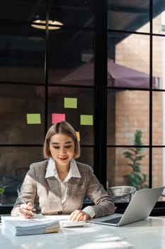 Young business woman checking paperwork from accounting department to analyse number on document, using computer laptop to check database.