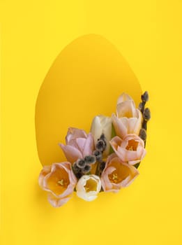 Creative Easter layout with fresh tulip flowers and leaves on bright yellow paper background. Spring natural concept. Shape in the form of an egg.