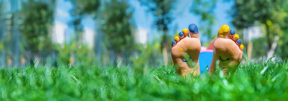 Child feet on the grass Ukrainian flag. Selective focus. Nature.