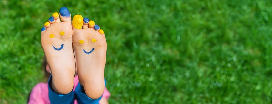 Child feet on the grass Ukrainian flag. Selective focus. Nature.