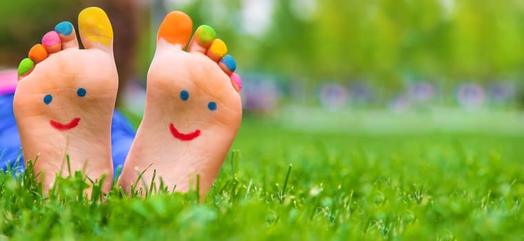 Feet of a child on the grass with a painted smile. Selection focus. Kid.