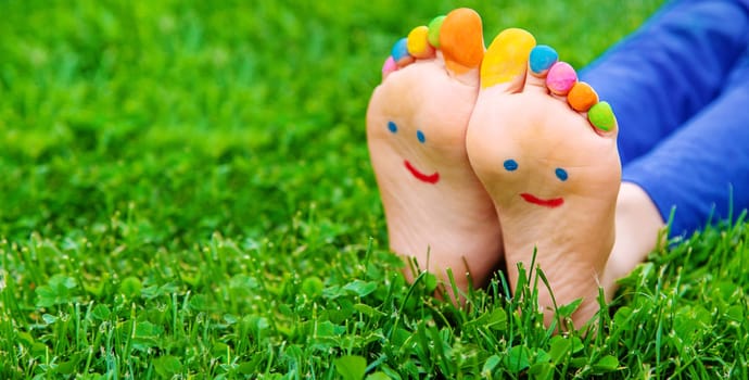 Feet of a child on the grass with a painted smile. Selection focus. Kid.