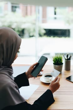 Beautiful Muslim woman shopping online using her phone and credit card.