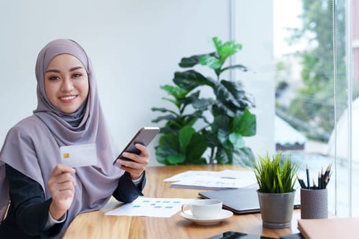 Beautiful Muslim woman shopping online using her phone and credit card.