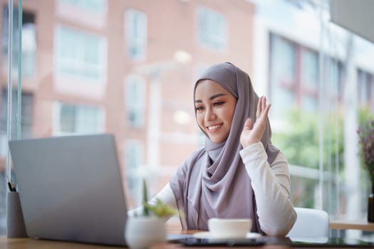 Beautiful Muslim woman using computer to greet attendees via video conference.