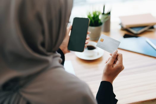 Beautiful Muslim woman shopping online using her phone and credit card.