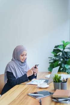 Beautiful Muslim woman talking on the phone and using a computer on her desk.