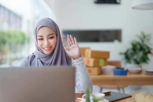 Beautiful Muslim woman using computer to greet attendees via video conference.