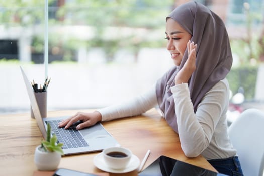 Beautiful Muslim woman using computer to greet attendees via video conference.