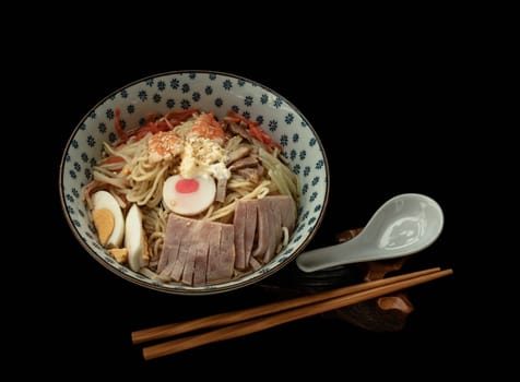 Cold noodles (Remen) with roast pork sliced, shrimp, ham, boiled egg and lemon sauce in blue ceramic bowl served with spoon and chopsticks on black background. Japanese style noodles, Healthy life style eating and Asian food concept. Space for text, Selective focus.