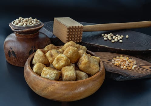 Brown fried tofu puffs or Deep Fried Tofu in wooden bowl and grains (soybeans) with dark background. Space for text.