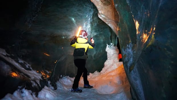 A girl with a neon lamp stands in an ice cave. The white light is highlighted with a bright orange light. Huge ice walls reflect the lantern. The color of the ice changes from dark gray to light.