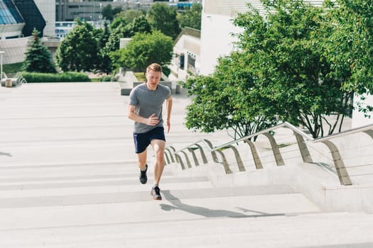 Young athlete man runner running up and down on city stairs in summer on morning run, background urban city street. Sports training. Fitness cardio workout in fresh air, walk outside.