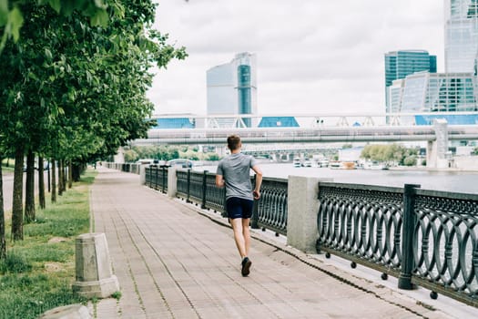 Young athlete man runner running at summer morning, background urban city street. Sports training. Fitness cardio workout in fresh air, jogging outside.