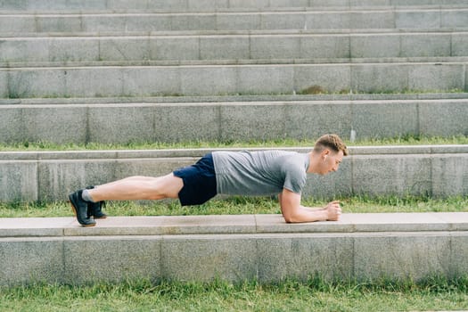 Young man has fitness workout. Male athlete does abs exercise, sport and training outdoor and stands in plank. People sport and healthy lifestyle concept.