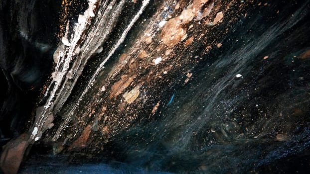 The black transparent color of ice in the cave. Small stones hang down in places. There are frozen air bubbles and grains of sand in the ice. Black-brown shade of ice. Deep in the glacier. Epic