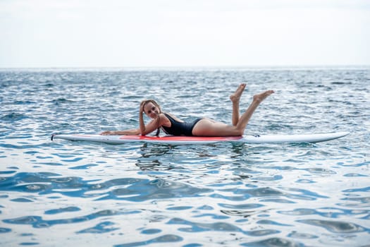 Woman sap sea. Sports girl on a surfboard in the sea on a sunny summer day. In a black bathing suit, he lies on a sap in the sea. Rest on the sea