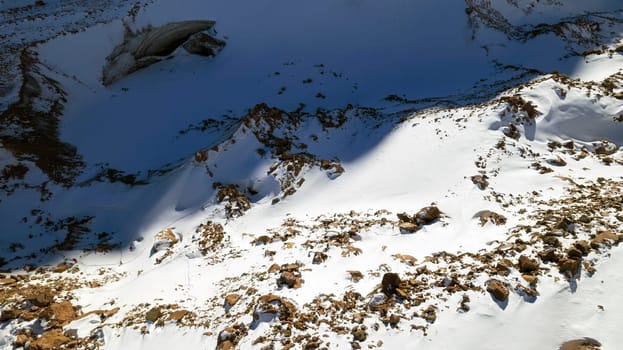 A huge frozen glacier in the mountains and a lot of tourists. Walking in the snow, taking photos with ice. Top view from a drone. Ice resembles marble. Dark light gray tones. Snowy mountains. Almaty