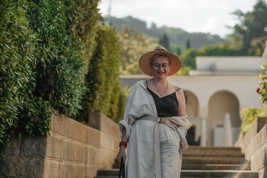 Woman on the stairs in the park. A middle-aged lady in a hat in a white outfit with a bag walks around the Livadia Palace.