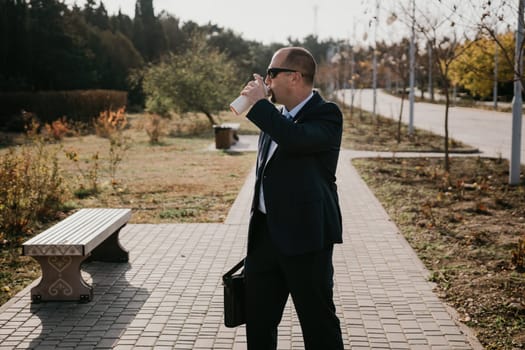 Mature entrepreneur drink coffee in autumn park. Senior executive rest in city park.