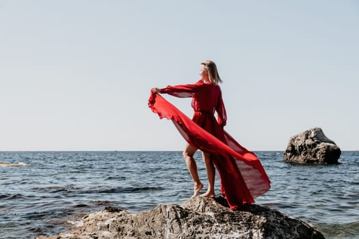 Woman travel sea. Young Happy woman in a long red dress posing on a beach near the sea on background of volcanic rocks, like in Iceland, sharing travel adventure journey